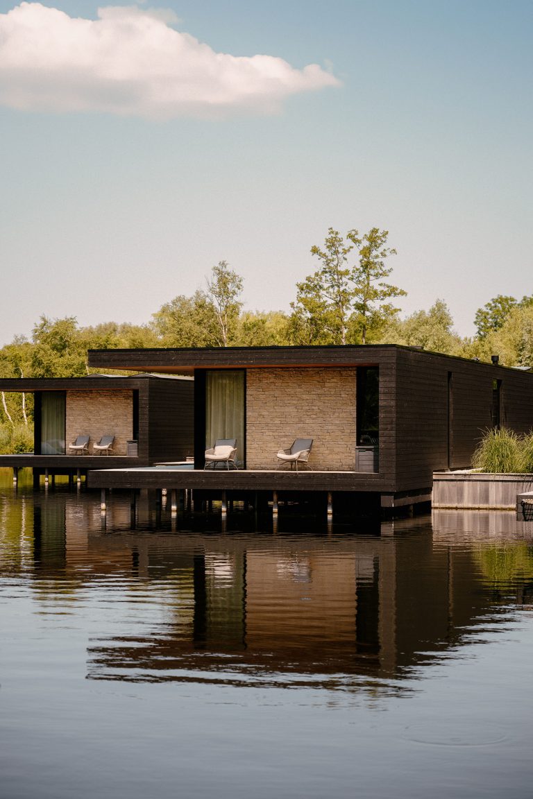 Moderne, nachhaltige Wasser-Villa mit Terrasse über dem Wasser, umgeben von Natur und sich in der ruhigen Oberfläche der Loosdrechtse Plassen spiegelnd