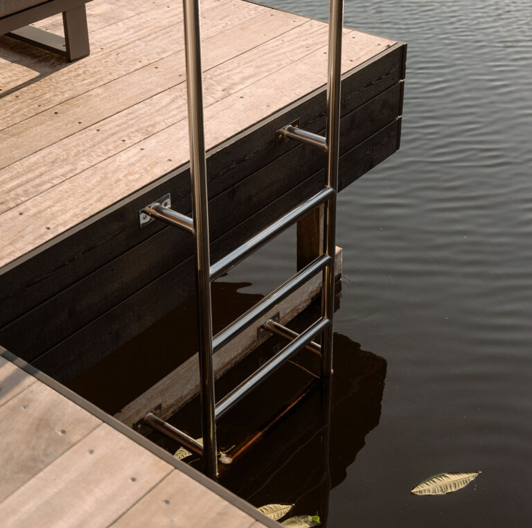 Detailansicht einer Holzterrasse mit Badeleiter am Wasser und luxuriöser Liege, direkt am Rand der Wasser-Villa