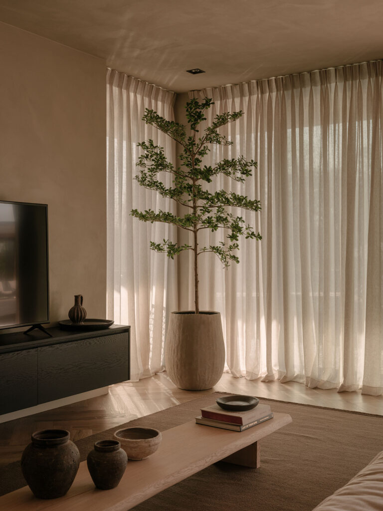 Eine gemütliche Ecke im Wohnzimmer mit einer großen Zimmerpflanze, weichen Leinenvorhängen, einem Couchtisch aus Holz und warmen Naturtönen für eine ruhige und nachhaltige Atmosphäre