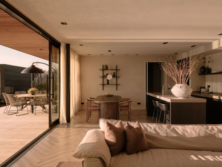 Geräumiges Wohnzimmer mit offener Küche, Essbereich und sanften Naturtönen, verbunden mit einer sonnigen Terrasse am Wasser für einen ruhigen und nachhaltigen Aufenthalt