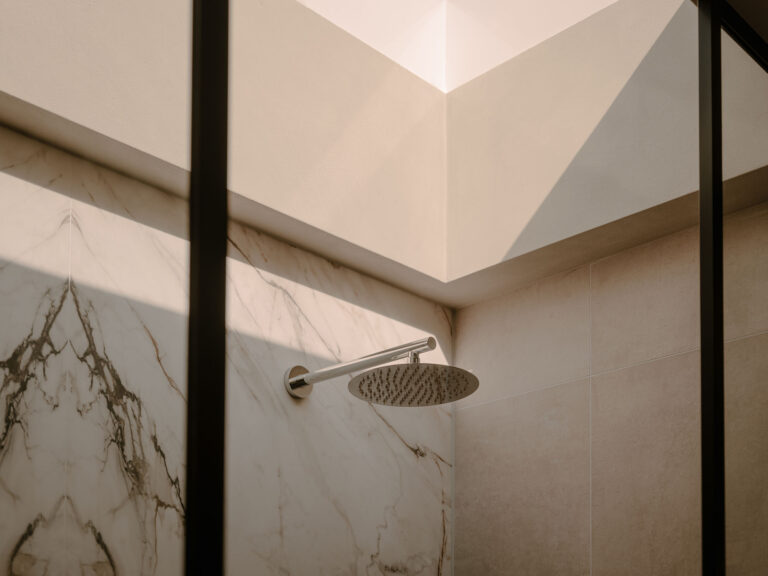 Detailansicht einer stilvollen begehbaren Dusche mit Regendusche, Wandverkleidung in Marmoroptik und natürlichem Tageslicht für ein ruhiges, luxuriöses und nachhaltiges Badezimmererlebnis