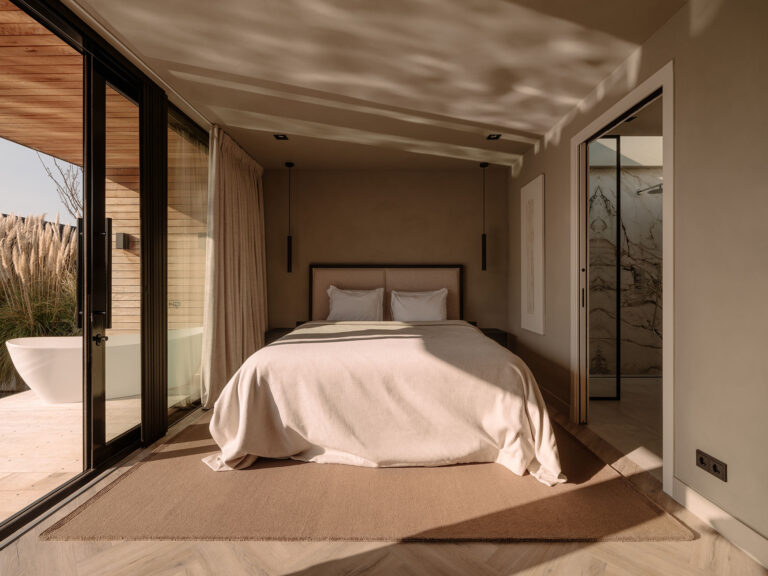 Ruhiges Schlafzimmer in Naturtönen mit großem Bett und Flügeltüren zur privaten Terrasse, verbunden mit einem stilvollen Badezimmer für einen luxuriösen und nachhaltigen Aufenthalt