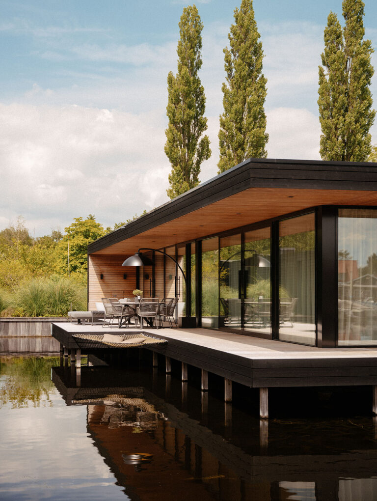 Moderne, nachhaltige Wasser-Villa mit Terrasse, Glasfassade und Sitzbereich im Freien direkt am Wasser, umgeben von Grün in einer ruhigen, natürlichen Umgebung