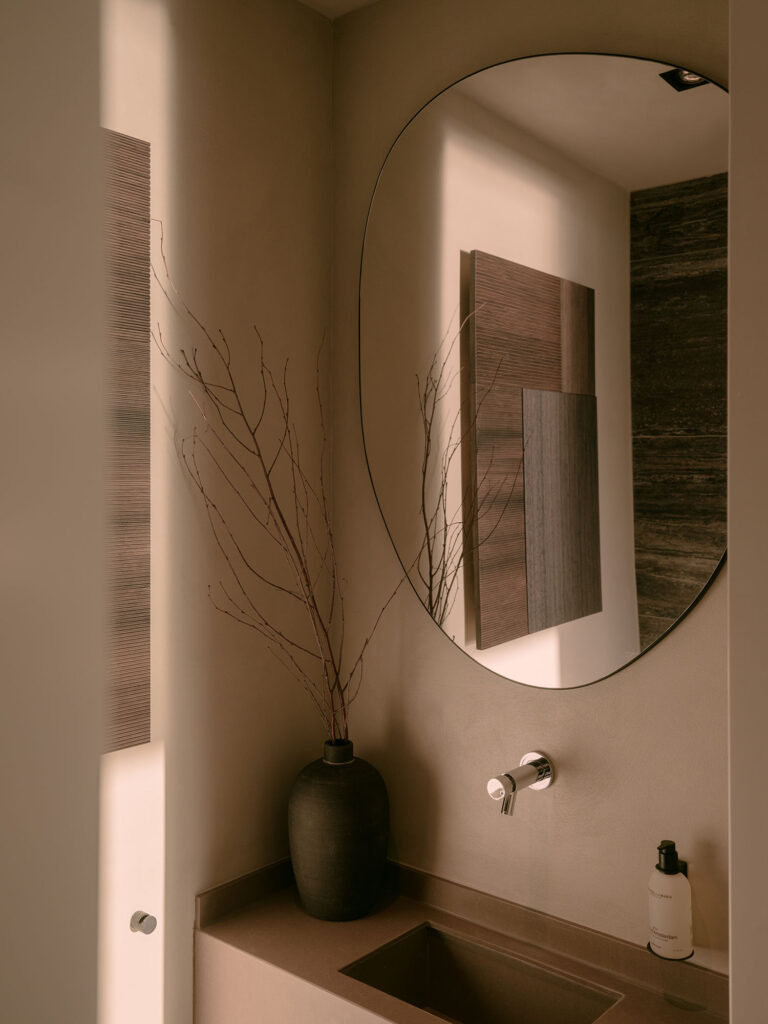 Ein stilvolles Waschbecken mit rundem Spiegel, minimalistischem Wasserhahn und dekorativen Accessoires in warmen Naturtönen und sanftem Licht