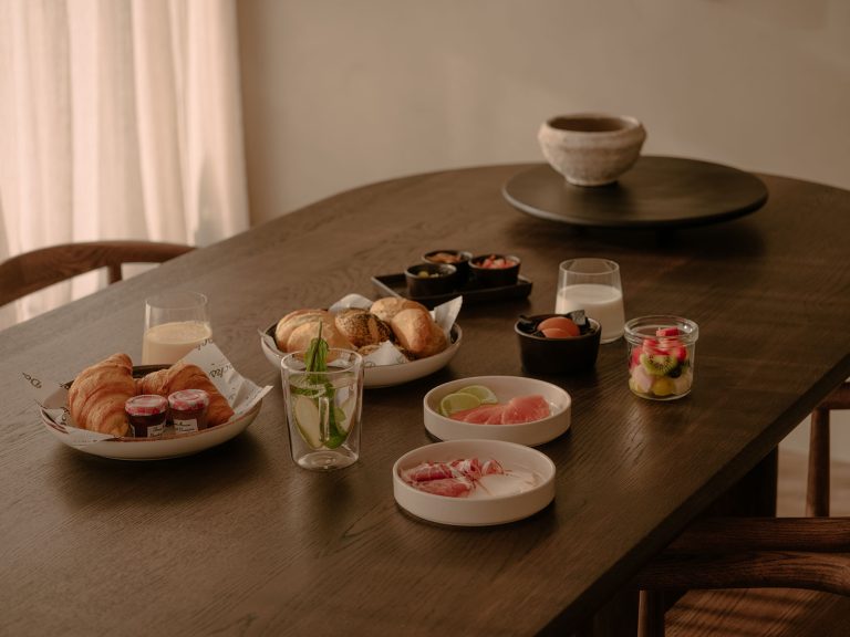 Ein stilvoll serviertes Frühstück mit frischen Brötchen, Croissants, Obst, Saft und Kaffee auf einem Holztisch in einer gemütlichen und ruhigen Villa