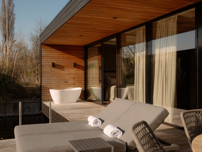 Luxuriöse Terrasse am Wasser mit Liegestuhl, Außenpool, Glasfassade und warmer Holzausstattung in einer stilvollen Wasser-Villa in einer ruhigen, natürlichen Umgebung