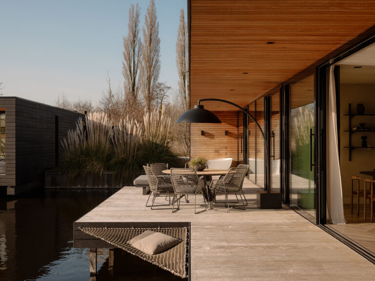 Holzterrasse am Wasser mit Esstisch, Loungemöbeln, Hängematte und Blick auf die Villa und die Schilfgürtel in einer ruhigen, natürlichen Umgebung