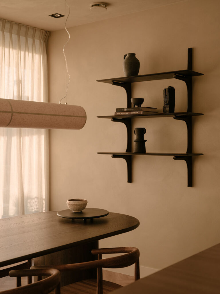 Stilvolle Essecke mit Holztisch, Designerstühlen, einer Hängelampe aus Leinen und einem Wandregal mit dekorativen Accessoires in warmen Naturtönen