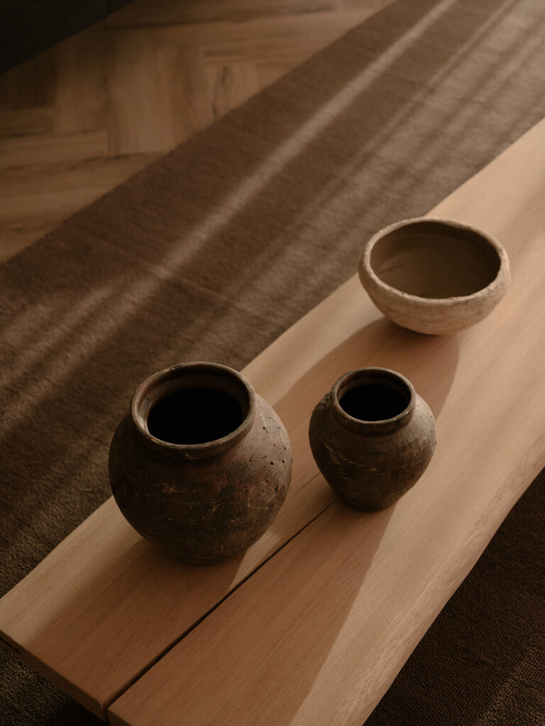 Detailaufnahme von Keramikaccessoires auf einem hölzernen Couchtisch mit warmem Lichteinfall und sanften Schatten in einer ruhigen, stimmungsvollen Villa