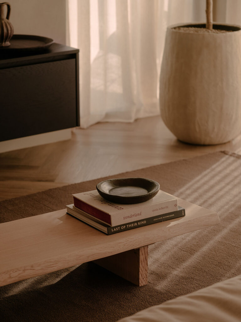 Detailansicht eines hölzernen Couchtischs mit Bildbänden und Accessoires, umgeben von weichen Stoffen, warmem Licht und natürlichen Materialien