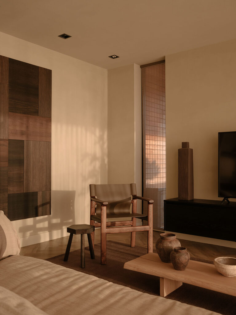 Gemütliches Wohnzimmer mit einem Holzsessel, Kunst an den Wänden, einem niedrigen Couchtisch und warmem Lichteinfall in einer ruhigen, stilvollen Villa